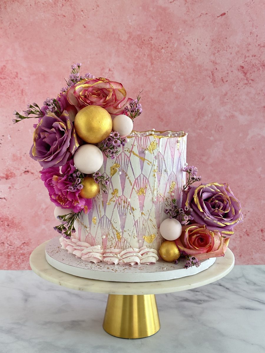 White two-tier wedding cake with burgundy roses and gold leaf