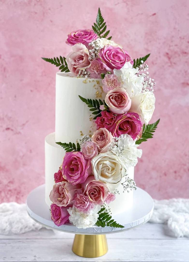White two-tier wedding cake cascading with fresh roses